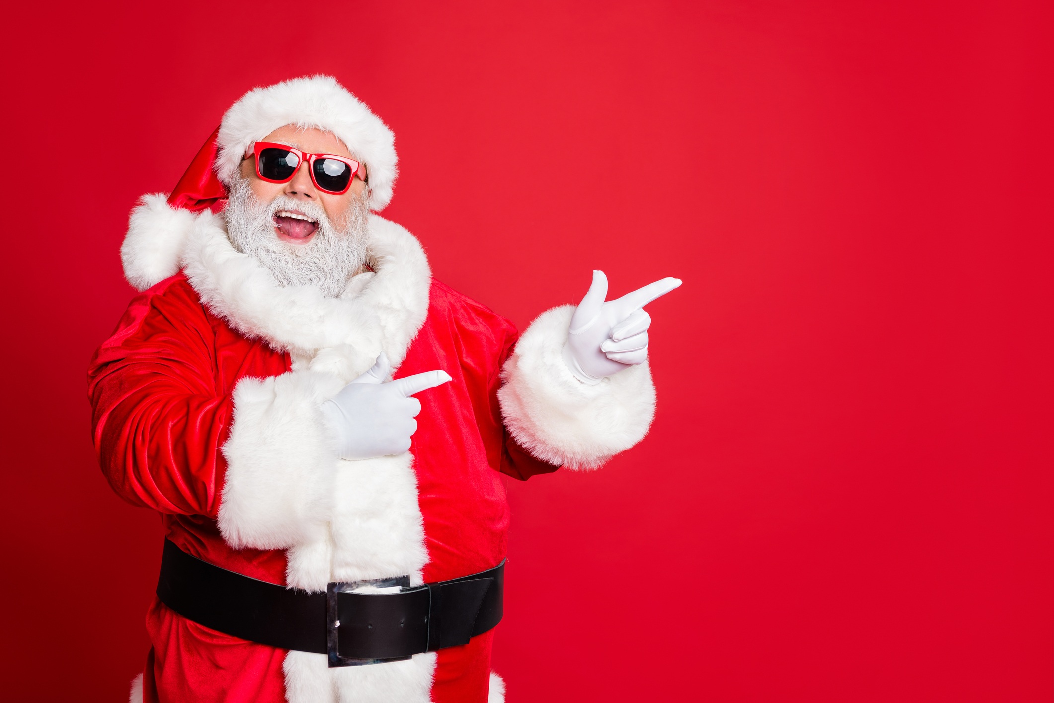 A man dressed as Santa wearing sunglasses, smiling and using both fingers to point to his left - Bee Digital Marketing