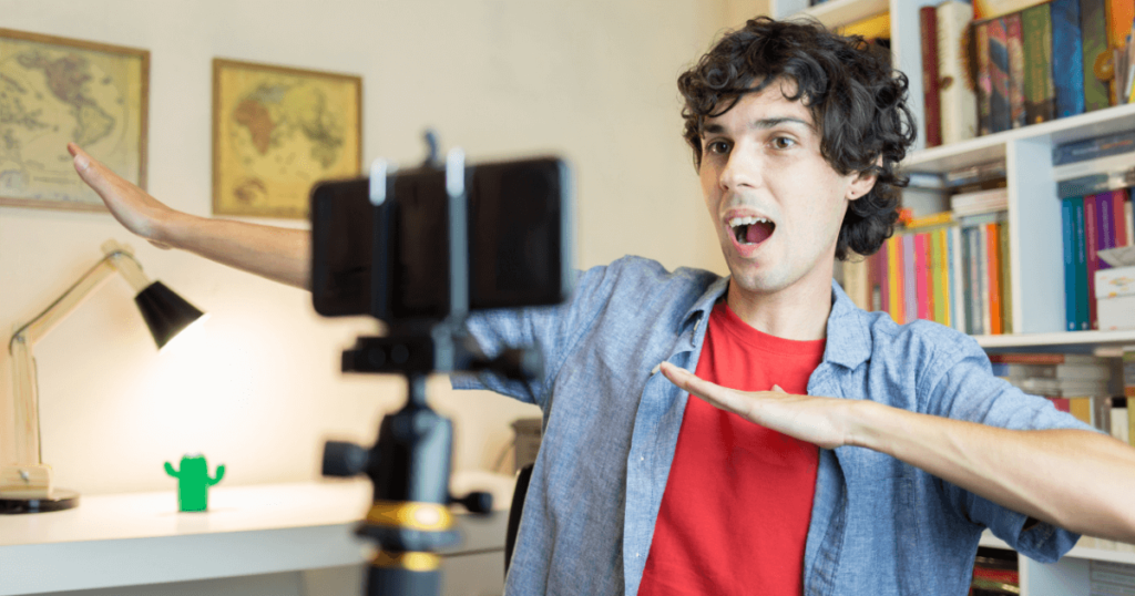 In the foreground is a mobile phone set up on a stand for a broadcast. In the background we see a man dabbing, performing on the broadcast.