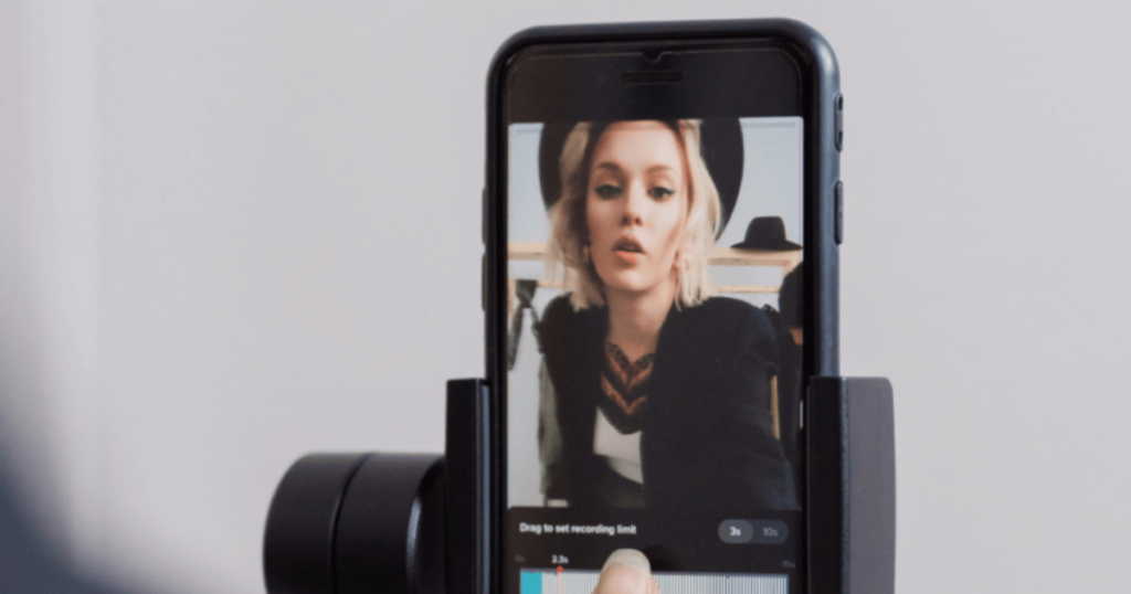 A mobile phone in a stand with a thumb touching the base, the picture shows that someone is recording a video of themselves speaking